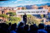 microsoft ceo satya nadella speaks to a crowd in front of a slide that says "leading in the new age of ai"
