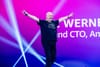 Amazon CTO Werner Vogels waves to the re:Invent 2025 crowd making two "V" gestures on stage.